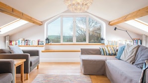 Quarto de loft aconchegante com um amplo claraboia, um banco embutido com livros, um lustre moderno e vista para o exterior.