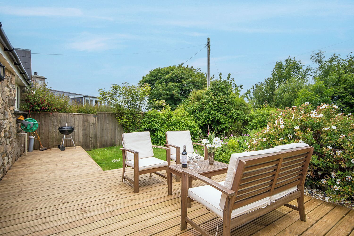 A wooden deck with outdoor furniture, a barbecue grill, and a garden with flowers and trees.