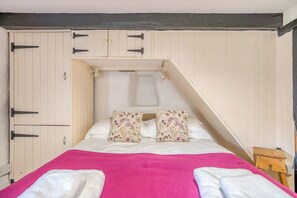 Une chambre à coucher avec un lit, des oreillers, une table de chevet en bois et une armoire.