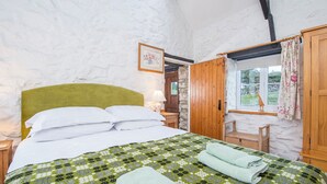 Une chambre confortable avec un lit, une tête de lit en bois, une fenêtre avec des rideaux et un mur en pierre.