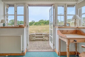 Une pièce avec une vue dégagée sur l’extérieur grâce à une porte ouverte, un radiateur, un bureau et une lampe.