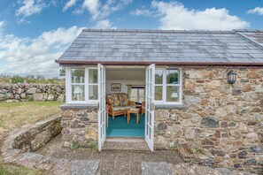 Une petite maison en pierre avec une porte ouverte donnant sur un espace extérieur aménagé.