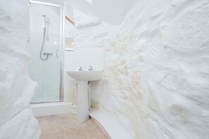 Une salle de bain dotée d’une douche à parois de verre, d’un lavabo sur colonne et de murs blancs à texture.