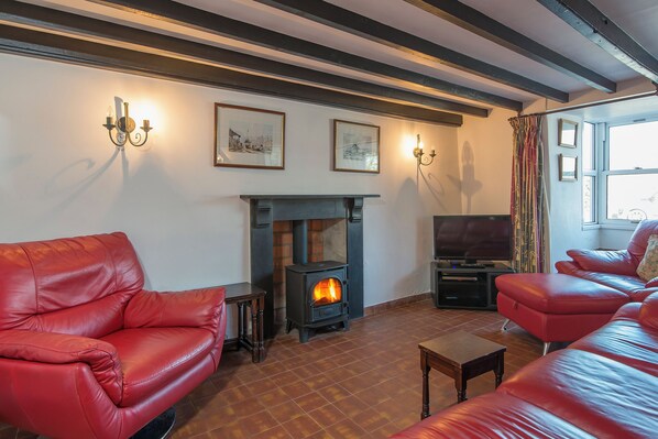 A living room with a fireplace, red leather sofas, a television, and framed pictures on the wall. - Ty y Mor, Holiday Cottage Newport, Sleeps 6, 3 bedrooms,  bathrooms (Newport)