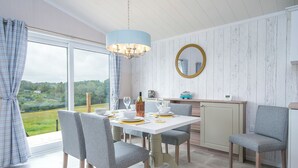 Un coin repas avec une table dressée pour quatre personnes, un lustre, un miroir et une vue panoramique par la fenêtre.