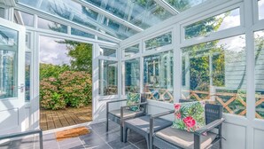 A conservatory with a glass ceiling, two wicker chairs with cushions, and a wooden deck outside. - Valley View, Holiday Cottage Little Haven, Sleeps 6, 3 bedrooms,  bathrooms (Haverfordwest)
