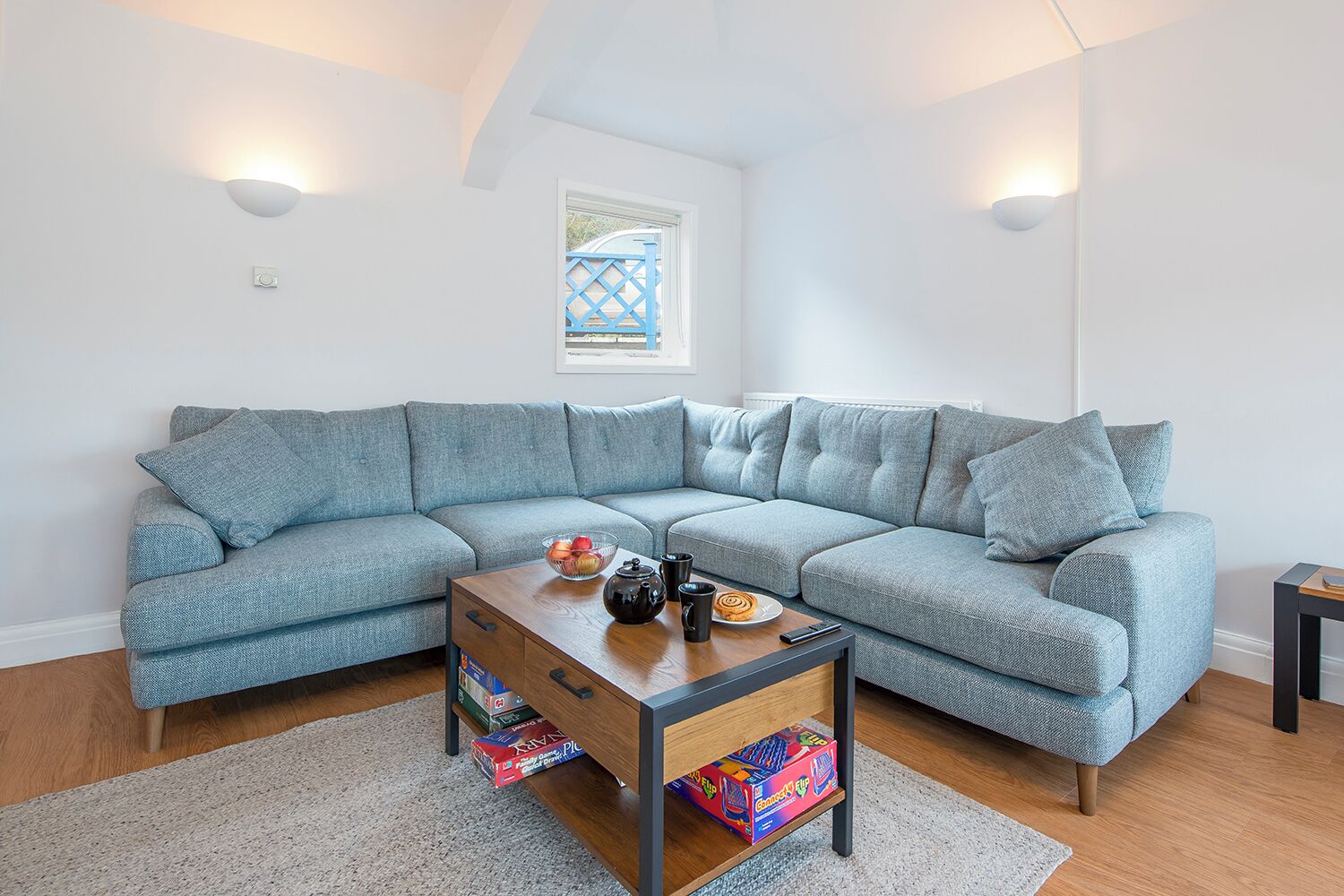 Een moderne woonkamer met een grijze modulaire bank, een houten salontafel en een bijzettafeltje.