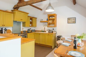 A kitchen with yellow cabinets, a wooden dining table set with plates and glasses, and a hanging light fixture. - Weavers Cottage, Holiday Property Llanmill, Nr Narberth, Sleeps 4, 2 bedrooms,  bathrooms (Nr Narberth)
