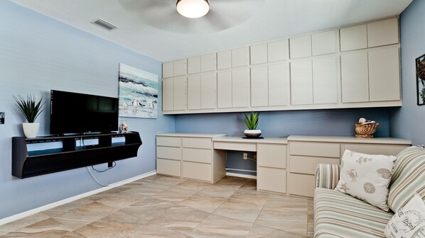 A compact living space with a flat-screen TV mounted on the wall, a small kitchen area with cabinets, a dining table, and a sofa with patterned cushions. - Boater’s Paradise with Pool Near Anna Maria Island (Bradenton)