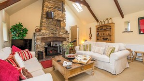A cozy living room with a stone fireplace, white sofas, a wooden coffee table, and a bookshelf.