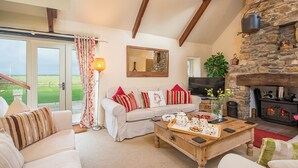 A cozy living room with a stone fireplace, a sofa set, a coffee table with snacks, and a TV.