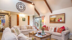A spacious living room with two white sofas, a wooden coffee table, and a large wall clock.