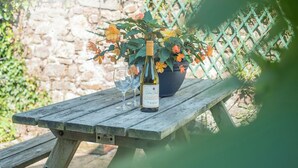 A wooden picnic table with a bottle of wine, two glasses, and a potted plant with flowers.