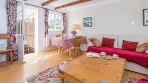 A cozy living room with a wooden coffee table, a red sofa, and a dining area with a checkered tablecloth.