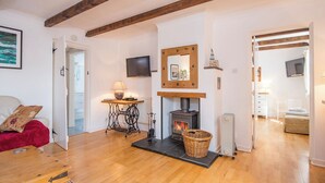 A cozy living room with a fireplace, wooden beams, a red sofa, a television, and a table with a lamp.