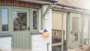 Une maison traditionnelle avec des portes et des fenêtres vertes, un mur extérieur blanc et une sphère orange et bleue suspendue.