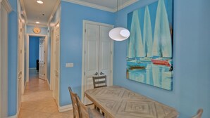 Un comedor con una mesa y sillas, una puerta blanca y un cuadro de veleros en la pared.