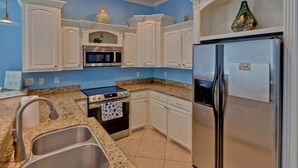 Una cocina con armarios blancos, un refrigerador de acero inoxidable, un microondas, un horno y encimeras de granito.