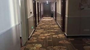 A hotel hallway with a patterned carpet, doors on both sides, and a fire extinguisher on the wall.