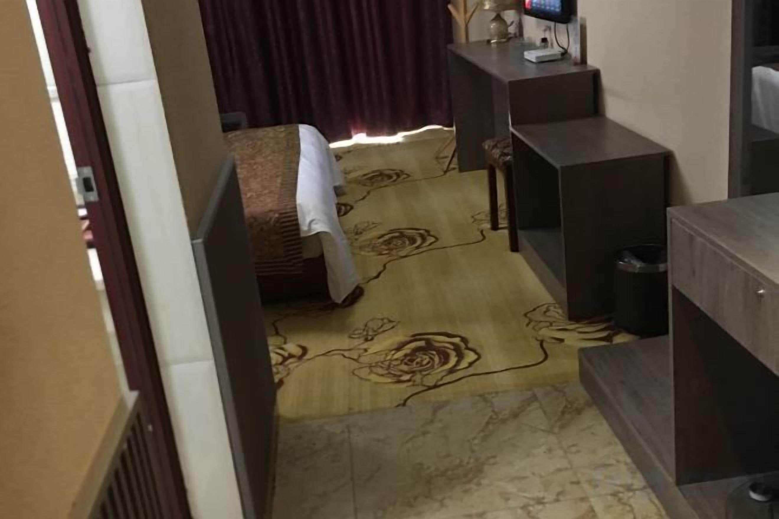 Habitación de hotel con cama, escritorio, silla, una mesita y alfombra estampada con motivos florales.
