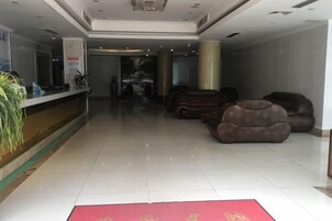 Un hall de hotel con mostrador de recepción, zona de estar y alfombra roja.