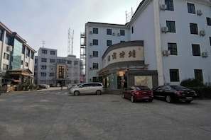 A building with a curved entrance, multiple floors, and several parked cars. - Jing'an Hostel (Jing'an)