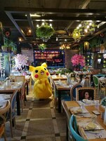 A restaurant interior with tables, chairs, hanging plants, and a large Pikachu mascot.