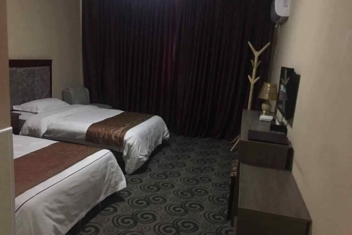 Habitación de hotel con dos camas, una cortina oscura, un escritorio con lámpara y un adorno en la pared.