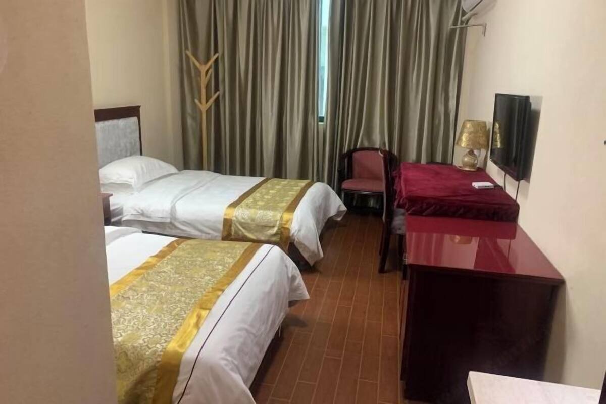 Habitación de hotel con dos camas, un escritorio, una silla, un televisor y una ventana con cortinas.
