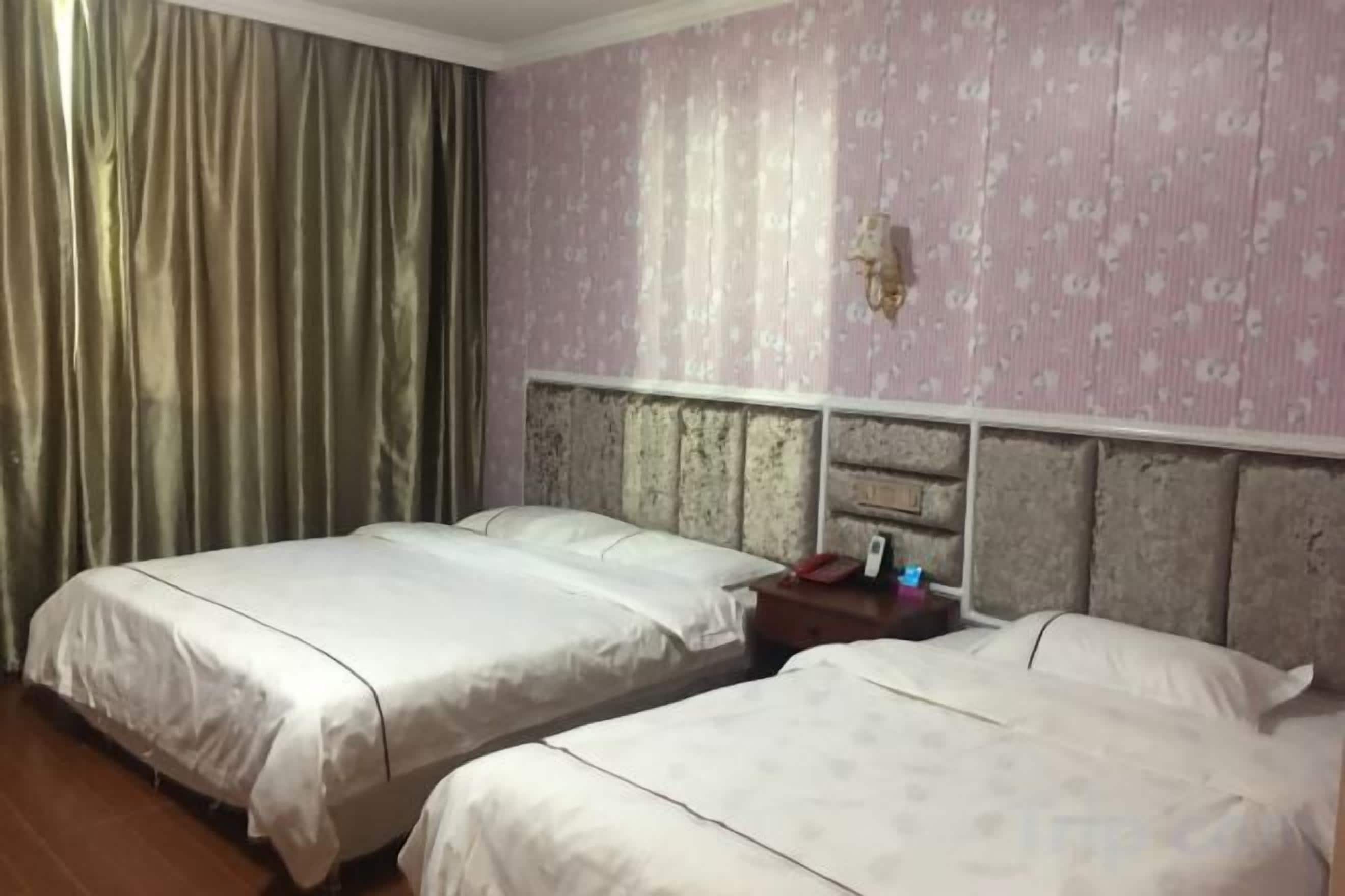 Ein Hotelzimmer mit zwei Betten, einem Kopfteil, einem Nachttisch und einem Vorhang.