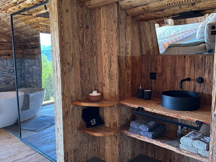 A rustic bathroom with wooden walls, a stone sink, and a bathtub.