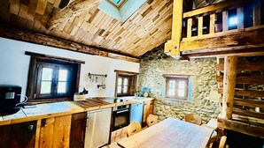 A rustic kitchen with wooden beams, a stone wall, and a wooden dining table. - Chasa Veglia (Scuol)