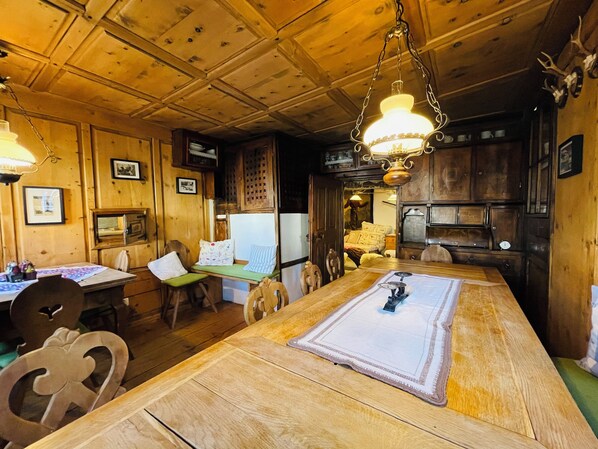 A wooden interior with a long dining table, chairs, and a hanging light fixture. - Chasa Veglia (Scuol)