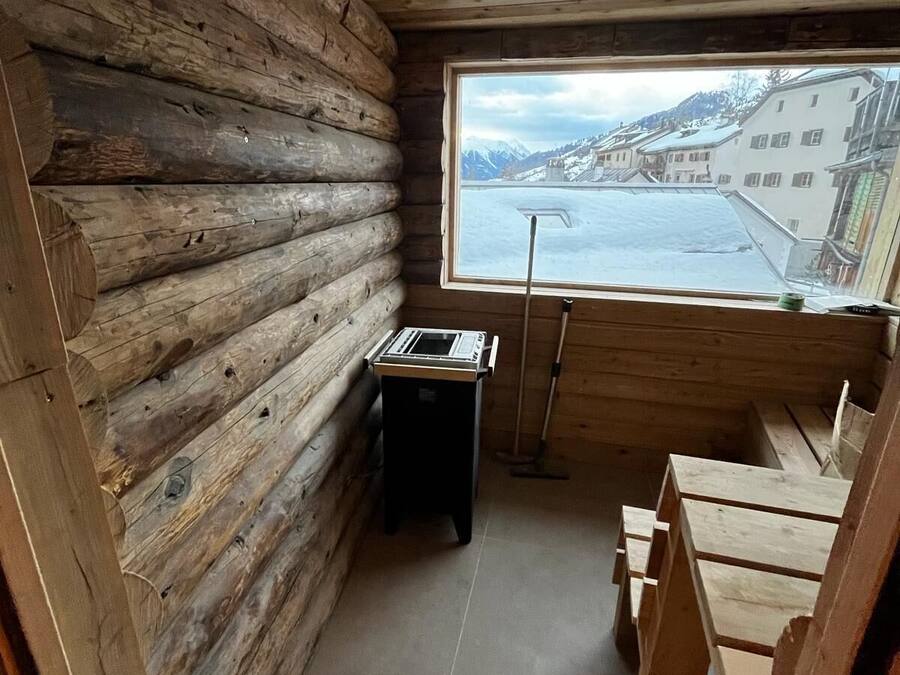 Una habitación tipo cabaña de troncos con ventana que da a un paisaje nevado y edificios.