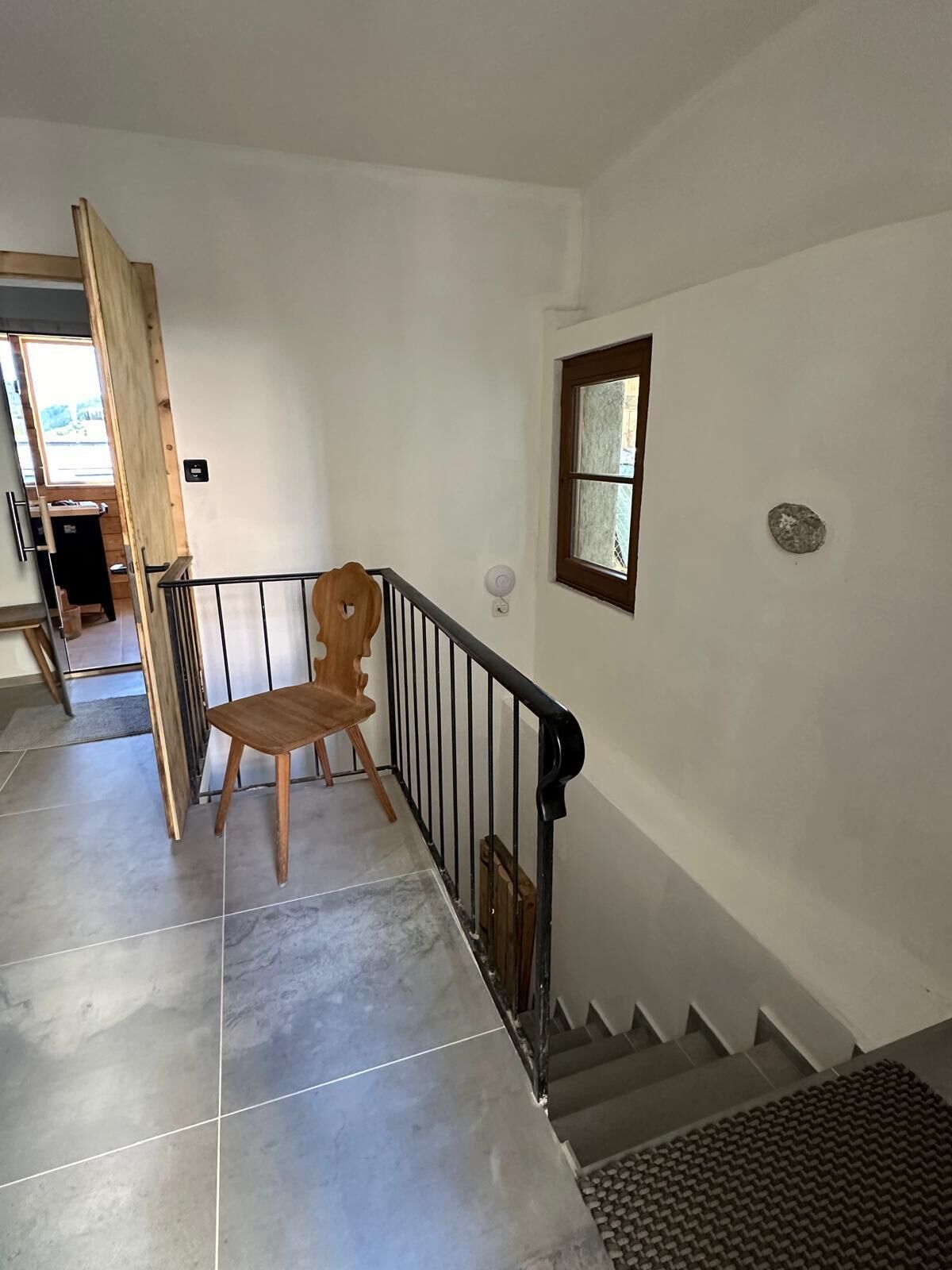Un escalier avec une chaise en bois placée au centre, une rampe en métal et une fenêtre donnant sur un paysage.