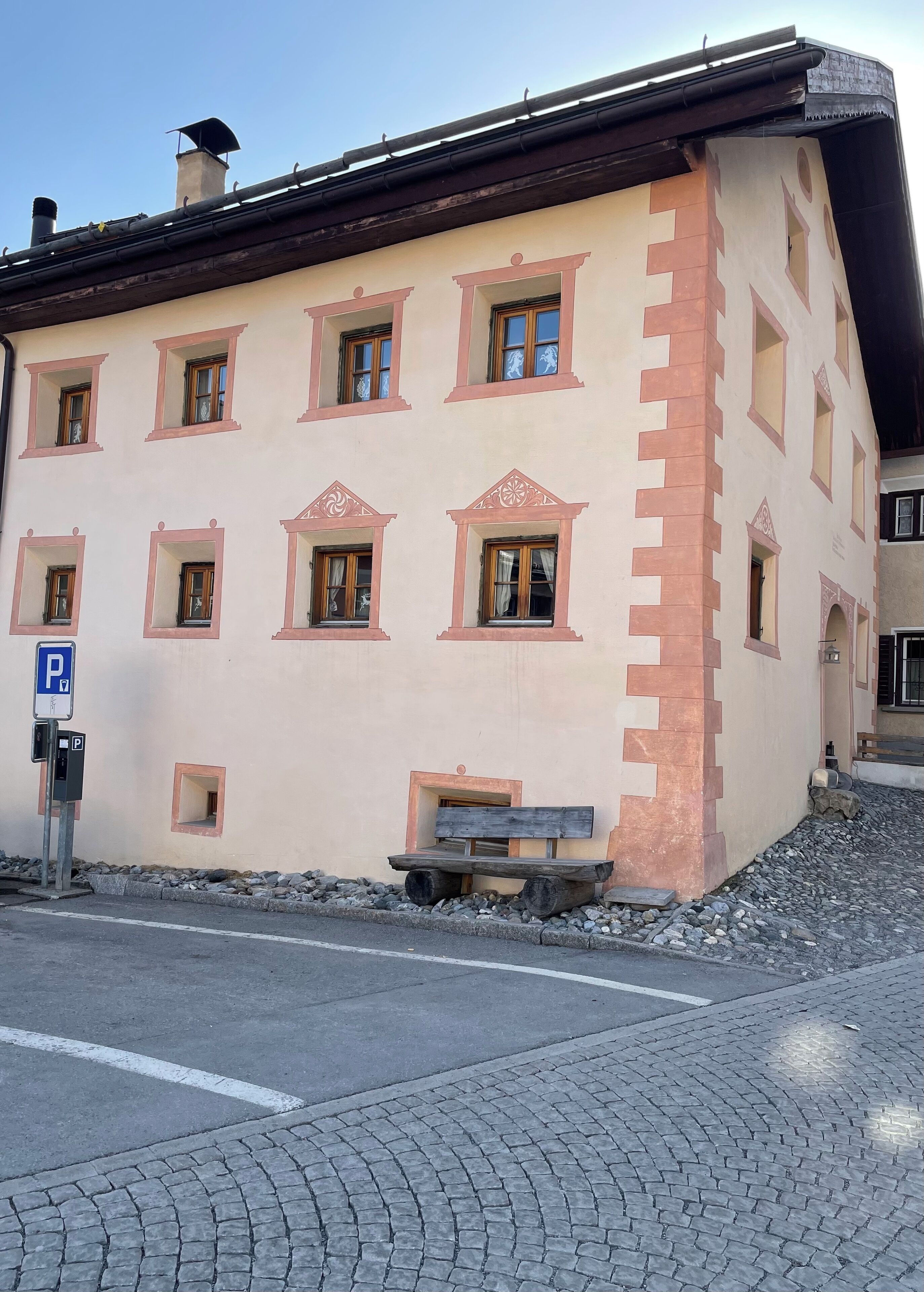 A building with multiple windows, a parking sign, and a bench.