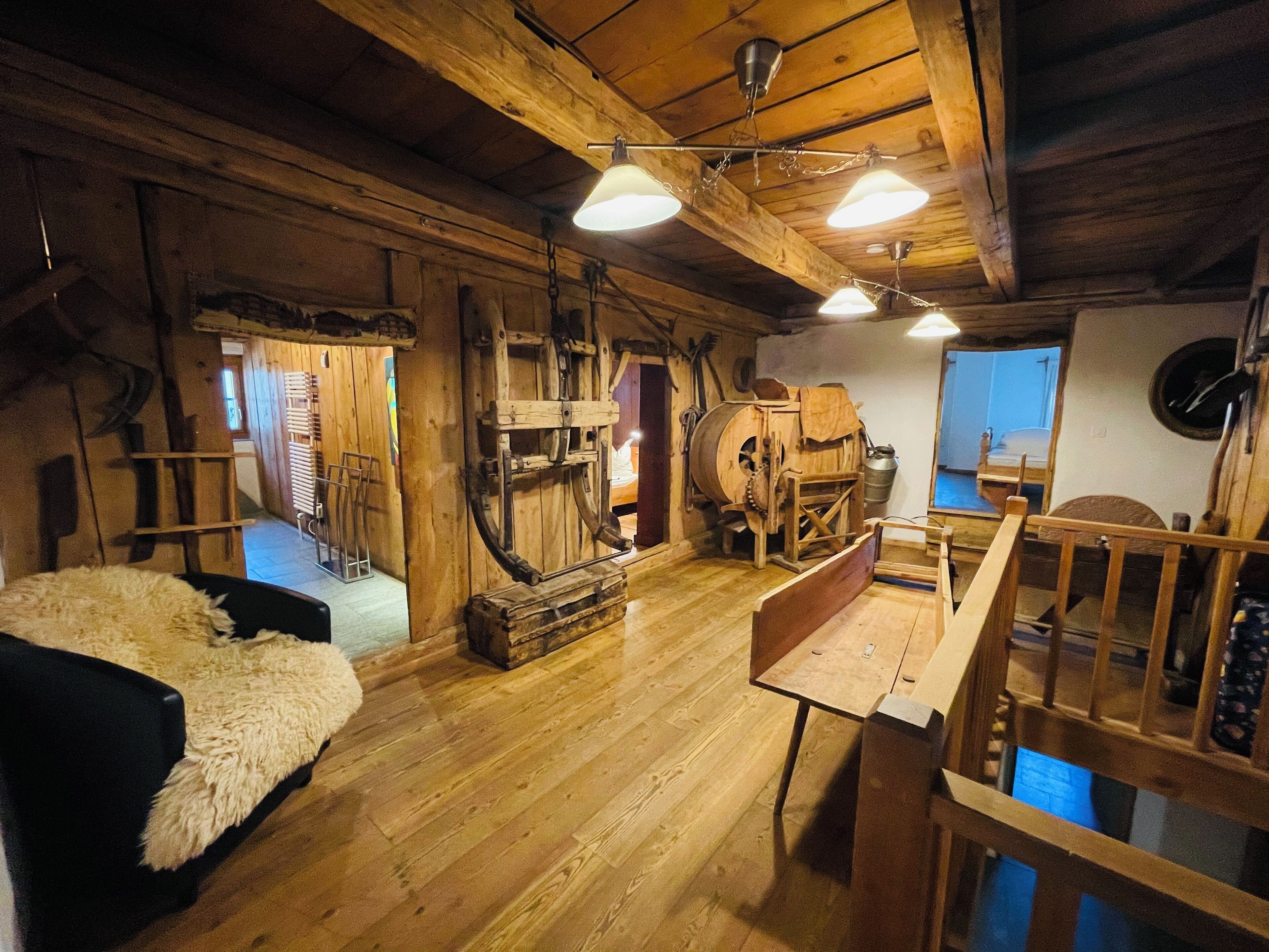 A rustic wooden interior with a wooden bed, a wooden table, and a wooden bench. There are wooden beams on the ceiling and a wooden wall.