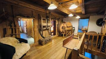 A rustic wooden interior with a wooden bed, a wooden table, and a wooden bench. There are wooden beams on the ceiling and a wooden wall.