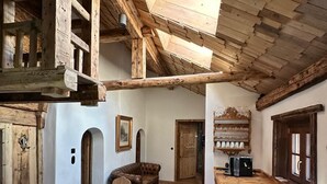 A rustic wooden interior with a high ceiling, wooden beams, a dining area with a wooden table and chairs, and a kitchen area with a countertop and appliances. - Chasa Veglia (Scuol)