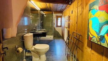 A bathroom with a toilet, bidet, and shower area. There is a painting on the wall and a window in the background.