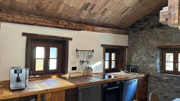A rustic kitchen with wooden beams, stone walls, and a wooden countertop.