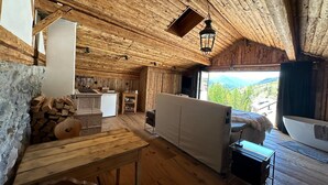 A rustic wooden cabin interior with a kitchen, dining area, and a large window offering a mountain view. - Chasa Veglia (Scuol)