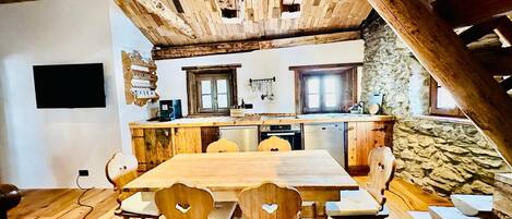 Une cuisine rustique avec des poutres en bois, un mur en pierre et un coin repas comprenant une table et des chaises en bois.