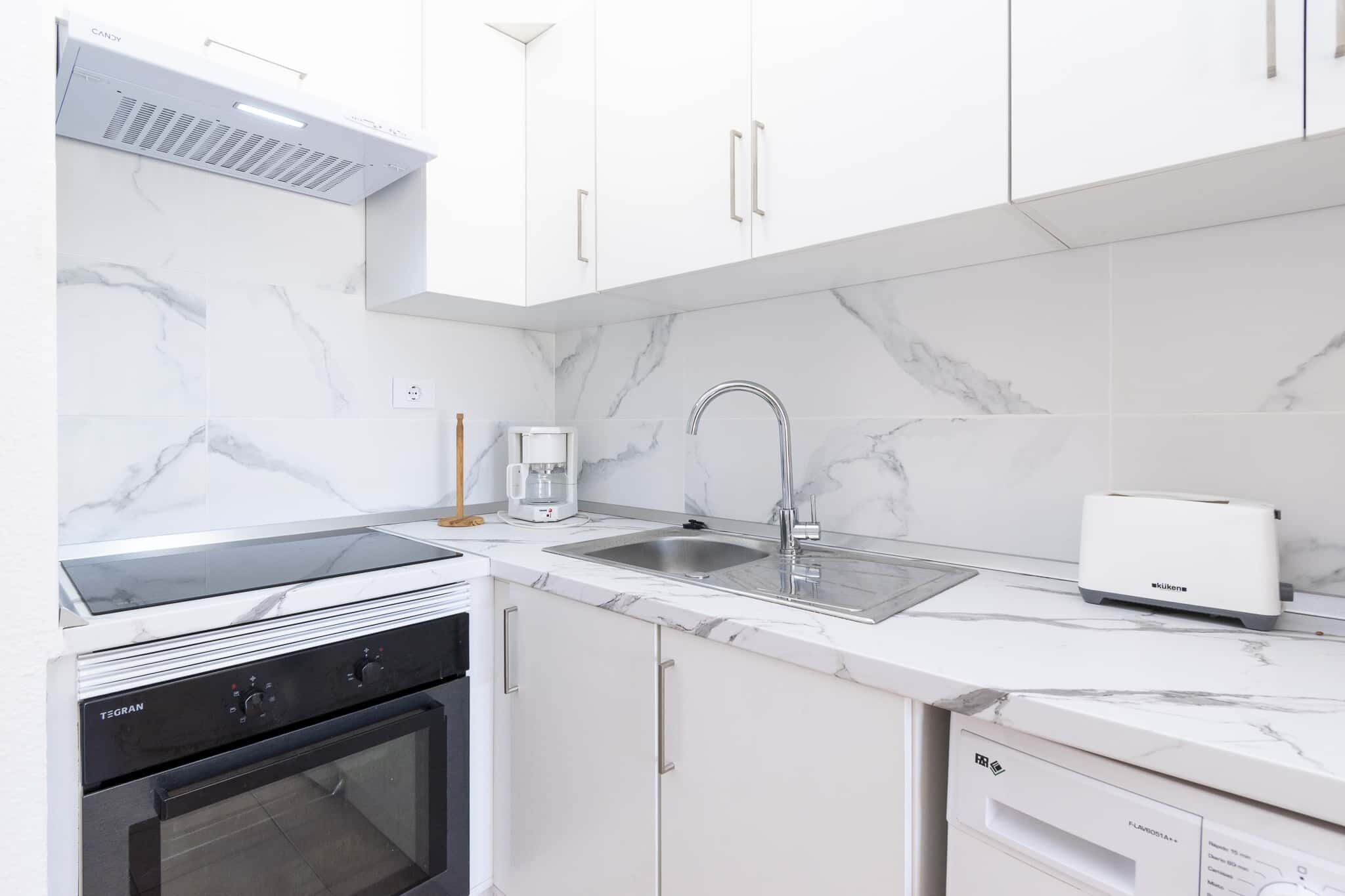 A modern kitchen with white cabinetry, a built-in oven, a coffee maker, and a dishwasher.