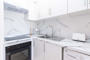 A modern kitchen with white cabinetry, a built-in oven, a coffee maker, and a dishwasher. - Castle Harbour 32 - One Bed (Los Cristianos)