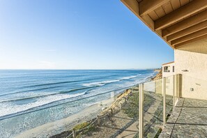 Een kustpand met een balkon dat uitkijkt over de oceaan, een pad van stenen en een gebouw met een beige gevel.
