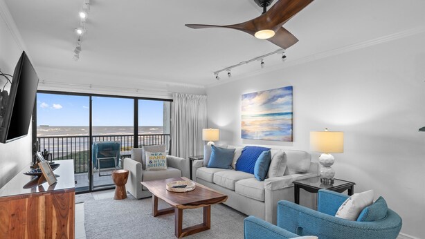 A spacious living room with a balcony, a ceiling fan, and a large window offering a view of the ocean.
