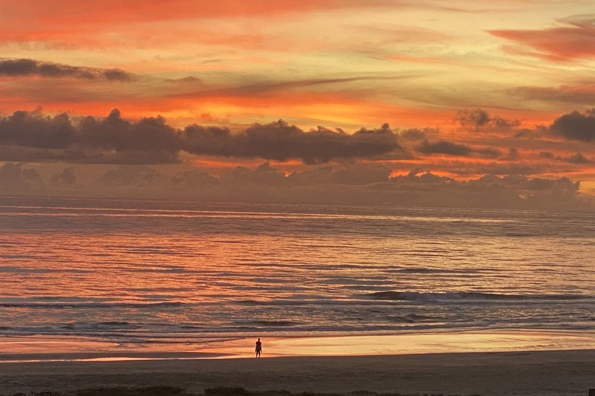 Une scène de plage où l’on voit une personne se promenant le long du rivage au coucher du soleil.