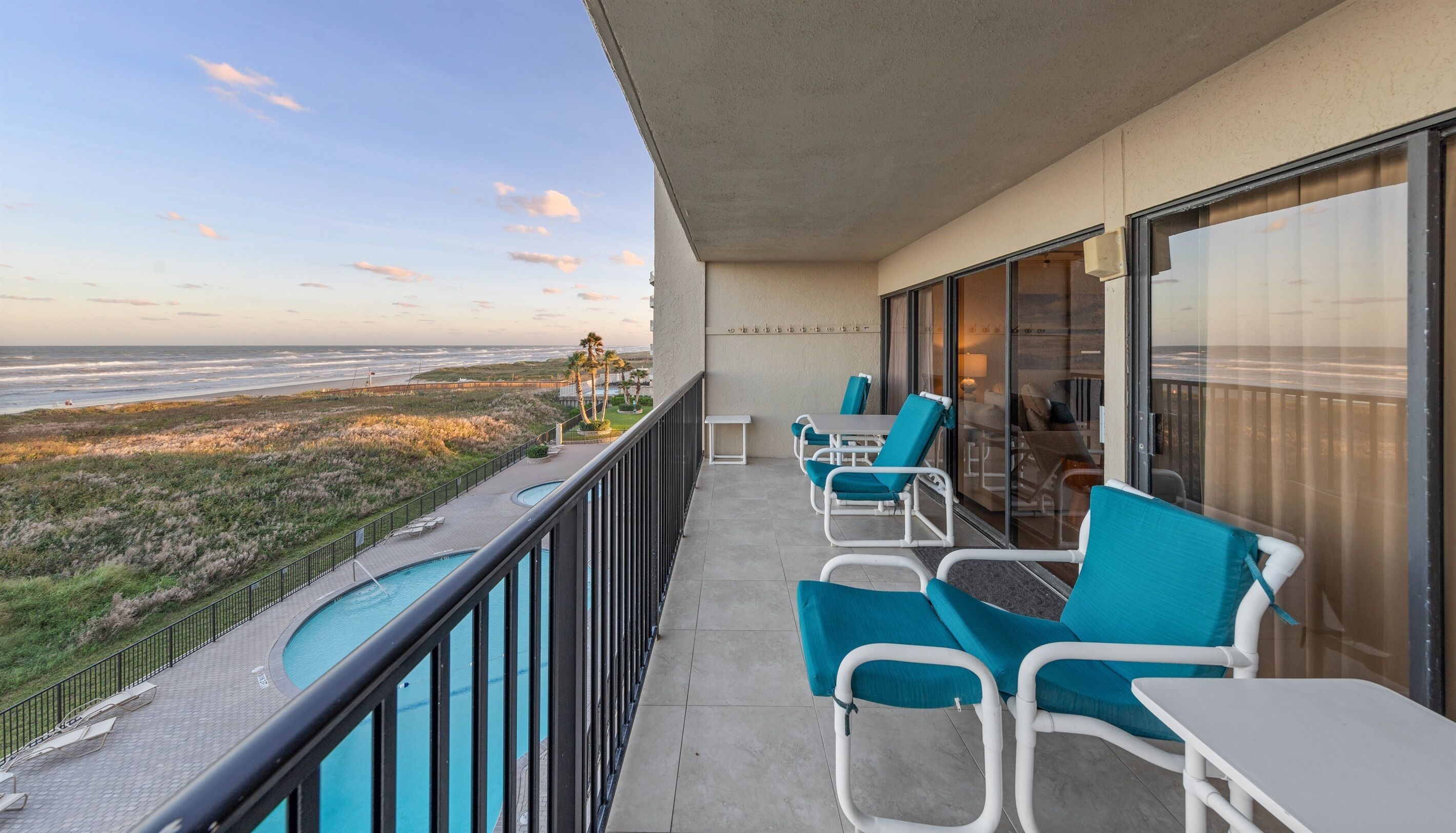 A balcony with a pool, chairs, and a view of the beach and ocean.