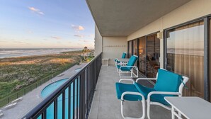A balcony with a pool, chairs, and a view of the beach and ocean.